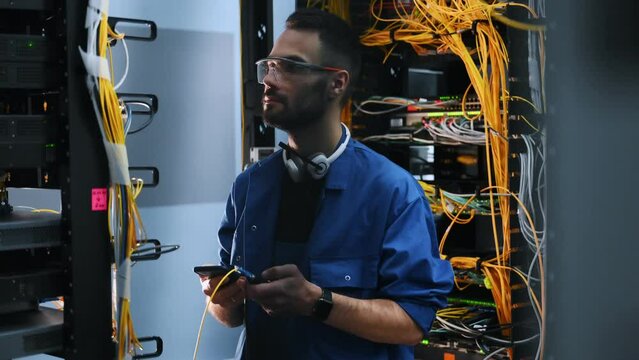 Professional device in hands. Young man is working with internet equipment and wires in server room.