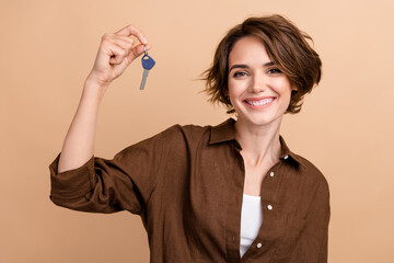 Photo of positive excited girl dressed brown shirt smiling rising new apartment keys isolated beige color background