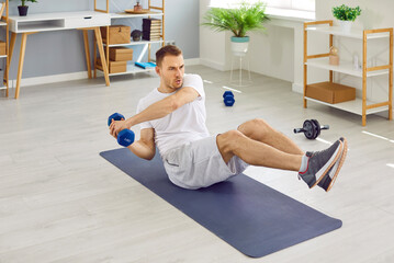 Fit, strong, young man sitting on a sports workout mat at home and doing an active fitness exercise...