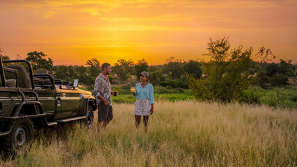 Asian women and European men on safari game drive in South Africa Kruger National Park. a couple of men and women on safari watching the sunset. Tourists looking sundowner with drinks on safari © Fokke Baarssen