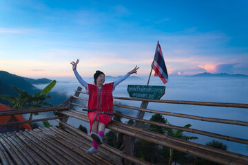 Asian traveler woman wearing a Red Karen Dress is happy with beautiful sea mist in the morning of mountain peaks the Thai language sign means Glor Selo Viewpoint of Mae Hong Son, Thailand.