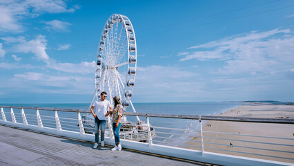 The Ferris Wheel The Pier at Scheveningen The Hague Netherlands on a Spring day, a man and a woman standing on the pier on the beach on a sunny day - obrazy, fototapety, plakaty