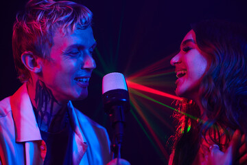 Happy young couple enjoying singing in karaoke in neon light