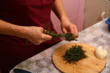 Crop anonymous female chef in uniform cutting fresh green parsley with knife on cutting board in kitchen
