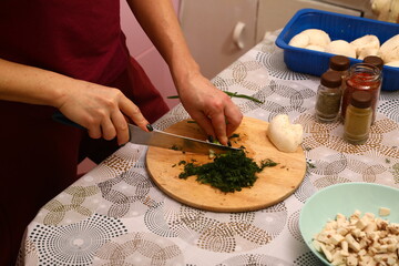 Crop anonymous female chef in uniform cutting fresh green parsley with knife on cutting board in kitchen
