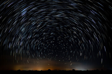 Abstract photo of Blue Night sky star trail background.Startrails on a dark blue sky at night,center sky area.Rotating star lines. The North Star and meteor showers. - obrazy, fototapety, plakaty
