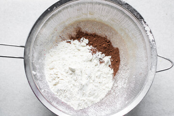 Sifting flour and cocoa powder for baking, a plastic sieve with flour and cocoa powder in it,...