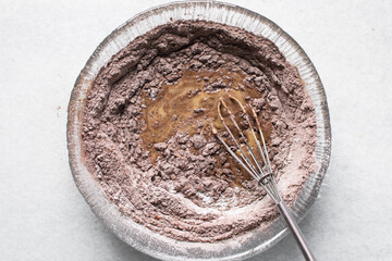 Chocolate muffin batter being mixed in a glass bowl, whisking cake batter in a glass mixing bowl,...