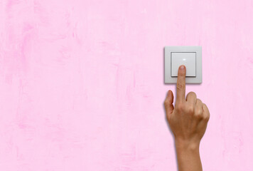 Female finger on light switch on pink coloured wall close up.