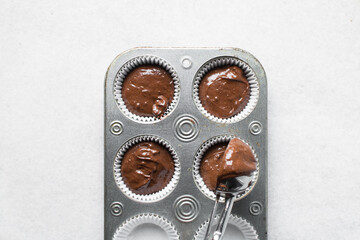 Scooping chocolate muffin batter into a cupcake tin, An ice cream scoop being used to portion...