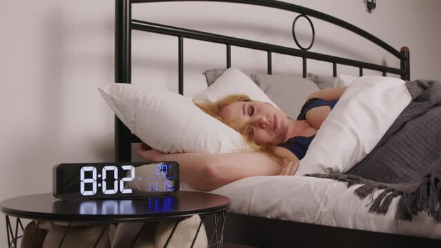 Shocked overslept pretty mature woman waking up too late , looking in panic at digital clock after missing alarm clock ring in morning , being displeased and frustrated .