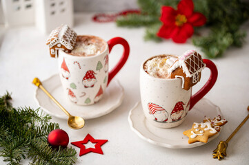 Obraz na płótnie Canvas Winter hot chocolate with marshmallows in a mug with marshmallow on a light background. Cozy still life with cocoa drink, cookies and decorations, gingerbread house, fir branch and poinsettia.
