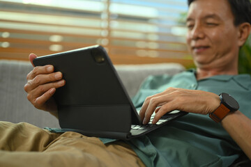 Cropped shot happy senior man watching video on digital tablet, sitting on couch at home.