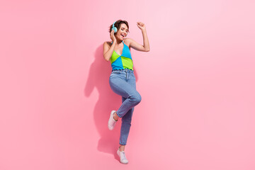 Full length cadre of charming hipster lady dance carefree touching her blue wireless earbuds loud sound isolated on pink color background