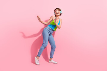 Full body photo of youth girl dancing feel comfy using light wireless headphones wear jeans and tank top isolated on pink color background
