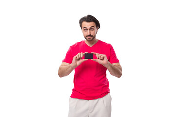 young brunette advertiser man dressed in a red t-shirt shows a plastic credit card