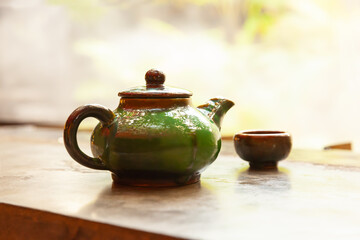 Obraz na płótnie Canvas Green ceramics teapot on wooden table with tropical behind in sunset light