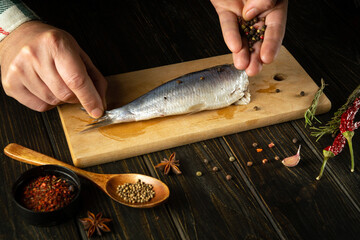 Cooking pickled herring with aromatic spices by the hands of a cook on the kitchen table. Fish diet...