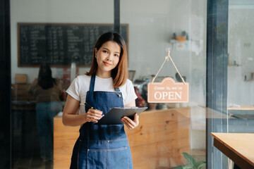 Young female hanging a welcome sign in front of a coffee shop. Beautiful waitress or hostess...