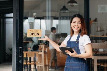 Young female hanging a welcome sign in front of a coffee shop. Beautiful waitress or hostess holding a tablet preparing in a restaurant..