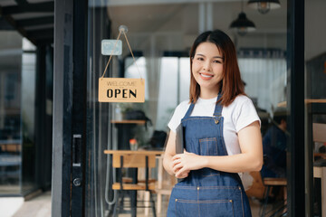 Young female hanging a welcome sign in front of a coffee shop. Beautiful waitress or hostess...