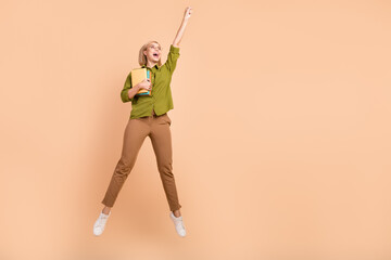 Full size photo of optimistic funny girl wear khaki shirt hold book raising fist up fly to empty...
