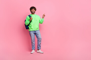 Full body photo of hipster guy wear backpack behind point finger empty space promoting education program isolated on pink color background