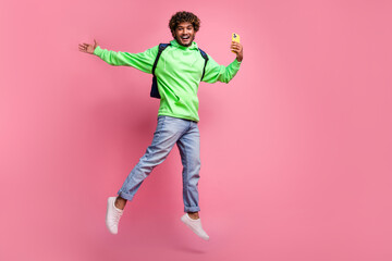 Fototapeta na wymiar Full body photo of guy jump hand demonstrating trendy mobile app using smartphone with rucksack behind isolated on pink color background