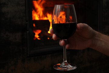Mans hand holds the wine glass in front of the fireplace. Blur burning fireplace background.