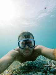 Diver in snorkeling goggles swims above the sea pebble bottom