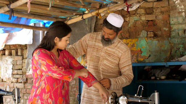 An Indian male tailor taking dress measurement for a female client - dress fitting . Muslim tailor at his tailoring workshop in a village shop - dress consultation  Indian small businessman  Indian...