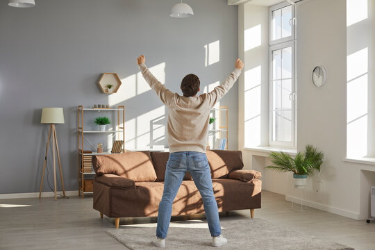 Finally alone at home. Man happy to have some free time for himself. Tired family man enjoys freedom while wife and children are away. View from behind funny man standing in living room with hands up