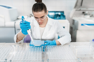 Young woman scientist working conducts research in modern bio laboratory. Female doctor laboratory assistant do tests, taking samples from test tubes with pipette - obrazy, fototapety, plakaty