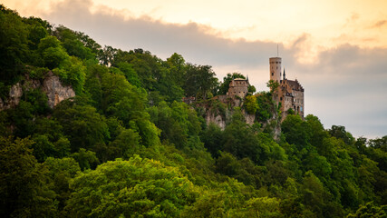 Panoramic view with Lichtenstein Castle located in Swabian Jura of southern Germany on a steep cliff overlooking the Echaz valley near Honau Reutlingen with warm sunset atmosphere on a summer evening. - obrazy, fototapety, plakaty