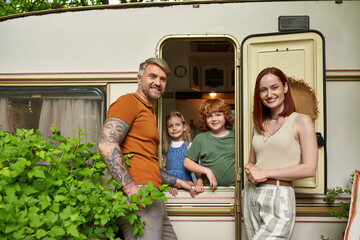 smiling parents looking at camera near happy children in trailer home, family leisure and recreation