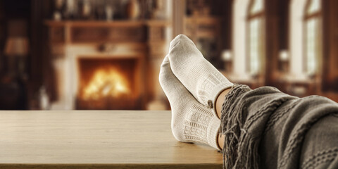 Woman legs with warm socks and home interior with fireplace. 