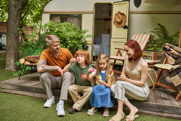 excited couple looking at children blowing soap bubbles near trailer home, leisure and fun