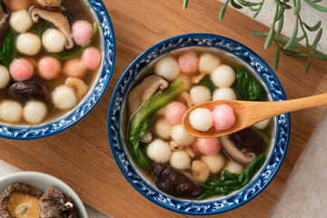 Eating homemade red and white small tangyuan with savory soup and vegetable.