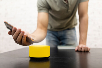 Man contacting with smart speaker musical column with voice assistant and his smartphone