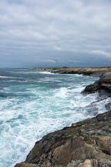 Obraz premium A dramatic seascape: turbulent waves crash against a rocky coastline under a cloudy sky, evoking nature s raw power