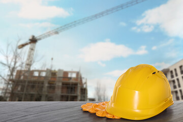 Safety equipment. Hard hat and gloves on wooden surface near unfinished building outdoors, space for text