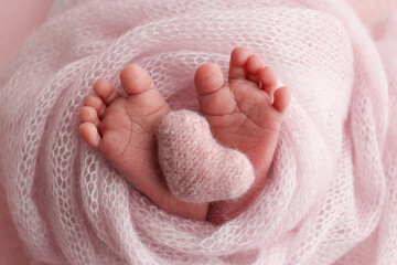 The tiny foot of a newborn baby. Soft feet of a new born in a pink wool blanket. Close up of toes, heels and feet of a newborn. Knitted pink heart in the legs of a baby. Studio macro photography.
