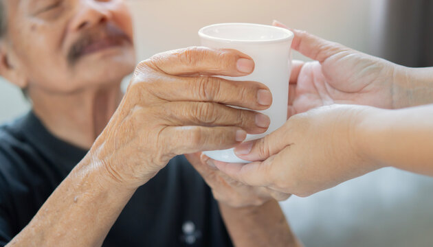 Cropped image hands of caregiver giving senior man with a cup of coffee or tea for breakfast in bedroom