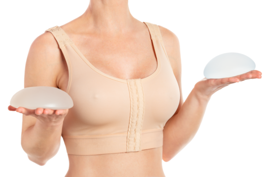 Woman holds round implants wearing compressing bra after breast augmentation.