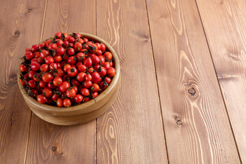red dog-rose rosehip fruits in a wooden bowl on wooden surface