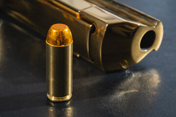 Close-up photo of a .50AE caliber cartridge and a gold color Desert eagle pistol.