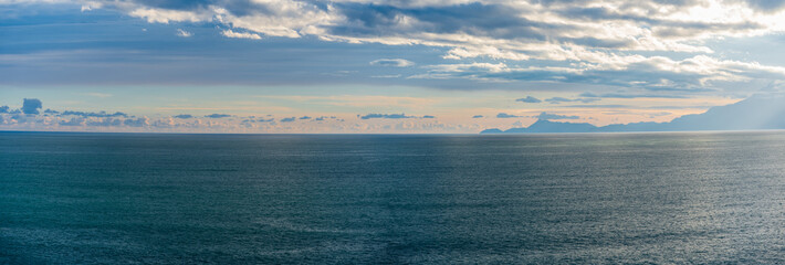 Wide-screen panorama of the sea and mountains with feathery clouds, a high-angle view.
