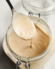 Tarator - Lebanese sauce from tahini with garlic, lemon juice and water. White or cream colored sauce in a jar on a marble background