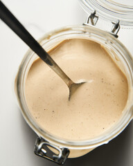 Tarator - Lebanese sauce from tahini with garlic, lemon juice and water. White or cream colored sauce in a jar on a marble background