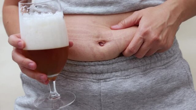 millennial woman drinking beer and eating potatoes chips.girl showing belly waist fat because of alcohol drinks.someone pouring beer into glass in front on face.doubts about eating apple or junk 